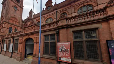 Google Exterior of Stourbridge Town Hall, a red-brick building with advertising posters for shows visible