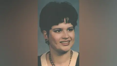 Suffolk Police A portrait shot of Karen Hales, who has dark hair and earrings and is wearing a necklace and a black top with a white top underneath. 