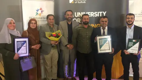Jon Wright/BBC Seven people stand with certificates and flowers at an awards presentation