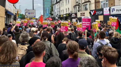BBC A large crowd of protesters gather in Walthamstow holding black lives matter and refugees welcome placards
