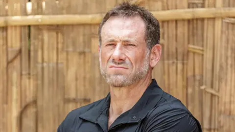 Channel 4 A publicity photo of Jason 'Foxy' Fox wearing a black shirt. He has a grey beard and short brown hair. He is pulling an intimidating face.