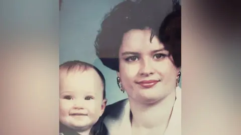 Hales Family A portrait showing Emily as a baby pictured with her mum Karen, who has black hair, earrings and red lipstick. 