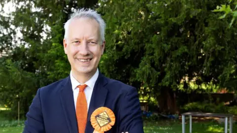 Liberal Democrats Gideon Amos wearing an orange rosette and matching tie