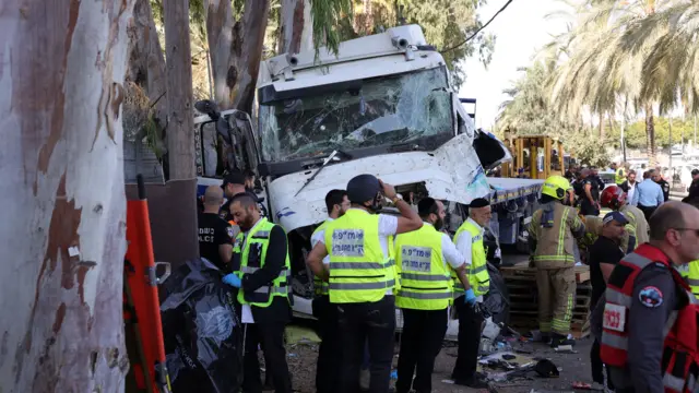 Image shows the front of a lorry with a smashed windscreen with emergency personnel in hi-vis working on the scene