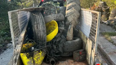 The SHIPS Project Rubbish, including large tyres, netting, plastics and rubber tubing, piled up in the back of a trailer. The trailer has metal panel on the sides and there is hedges in the background.