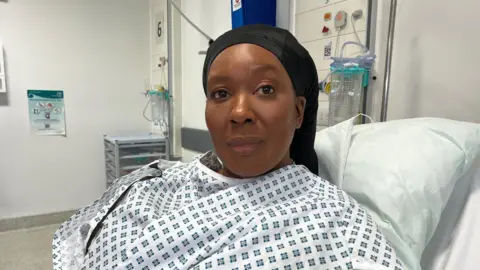 BBC Lieon Pemberton sits up in a hospital bed, wearing a hospital gown.