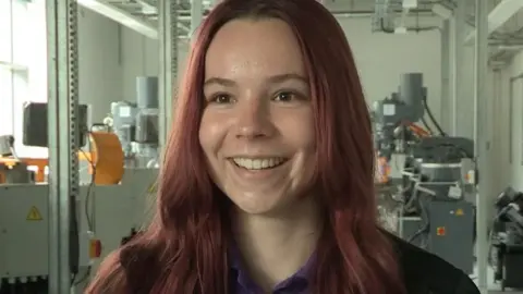 LDRS Ellie Ford, with reddish hair, is pictured standing in front of machinery at the institute
