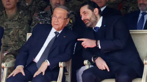 Reuters Lebanese President Michel Aoun (L) speaks to caretaker Prime Minister Saad Hariri (R) at a military parade on 22 November 2019