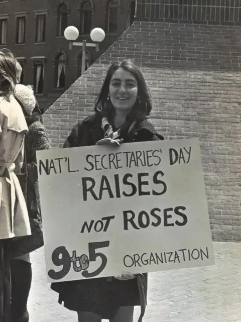 Karen Nussbaum Karen Nussbaum at the first National Secretaries' Day protest in Boston 1974, carrying a placard that says Raises not Roses