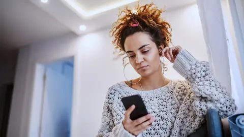 Getty Images Young woman using mobile phone at home