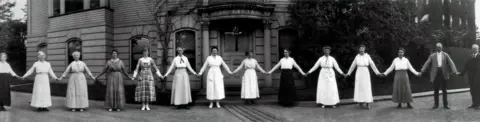Courtesy Harvard College Observatory, Plate Stacks A dozen women computers hold hands in this 1918 photograph, which Smith Zrull calls the "paper doll" photo. To the far right is Edward Pickering, who hired the women computers.