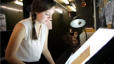 Alex Newman/PRI Curator Lindsay Smith Zrull places a glass plate photograph of a section of the sky onto a lightbox
