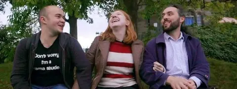 Three people sitting, holding hands
