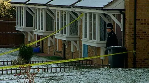 Police tape outside the house of Karen Hales in 1993. There is a police officer in front of the door and snow on the ground.