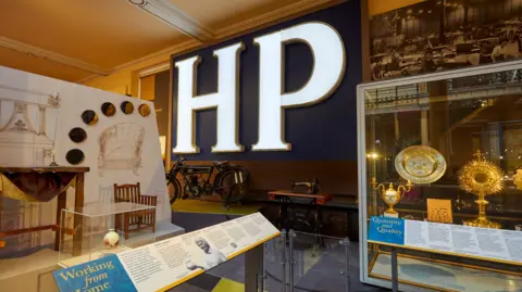 David Rowan The letters HP are lit up on a wall with various other items in cabinets in the museum on display around it