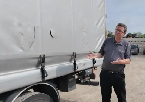 A haulier shows the side of his lorry curtain, which has been repeatedly torn with knife slashes in attempted thefts.