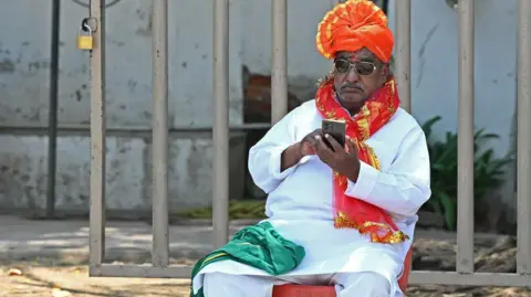 Getty Images A supporter of Bharatiya Janata Party (BJP) uses his mobile phone before a roadshow by BJP candidate ahead of the second phase of voting for country's general elections, in Hyderabad on April 24