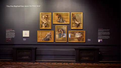 David Rowan Five portraits in yellow/gold frames are hung on a dark-coloured wall. On either side of them there is white writing on the wall, the writing is too small to read