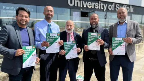 Jon Wright/BBC Five men of Bangladeshi heritage stand holding A4 posters promoting an awards event