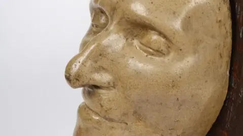 Ancient House Museum A mask made of yellowed plaster of Thomas Paine's face mounted on dark wood.