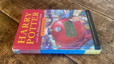 Rare Book Auctions A first-edition copy of Harry Potter and the Philosopher's Stone on a wooden table.