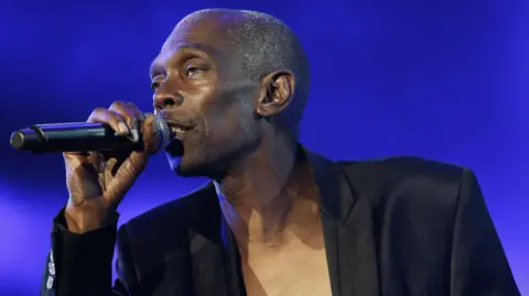 PETER KLAUNZER/ EPA-EFE/REX/SHUTTERSHOCK A man is pictured singing into a microphone he is holding in his right hand. He is wearing a black blazer with no shirt underneath.