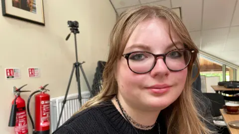 BBC A young woman with blond hair, wearing glasses.