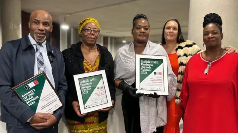 Jon Wright/BBC Clem Turner, Veronica Akrofi, Beverley Uter, Lydia Forrester and Angelina Quamina MBE from the Caribbean and African Community Health Support Forum - standing inside the University of Suffolk holding award certificates.