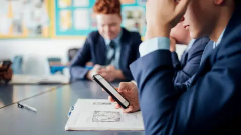 Getty Images Stock image of schoolboy using smartphone in class