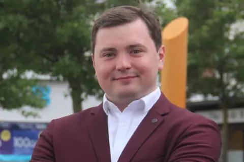 Labour Party Labour candidate Tom Plater in a burgundy-coloured suit and white open-neck shirt