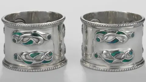 MNH A pair of silver napkin rings embossed with a Celtic interlocking design in green and turquoise.