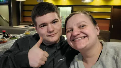 Sarah Sissons A selfie of Sarah Sissons wearing a grey sweatshirt with her son Ryan, holding a thumbs-up pose and wearing a grey hoody