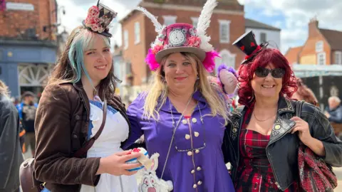 Amber Macey/BBC Three women showing off their steampunk outfits which comprise of brightly-coloured hats - one with a clock face in the centre
