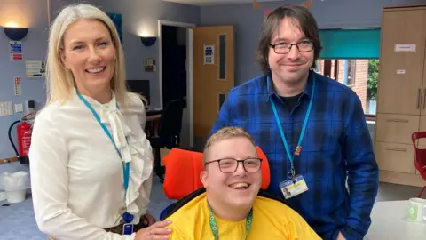 National Star College Lynette Barrett with her hand on Xenon's shoulder, with carer David Stokes standing next to him.