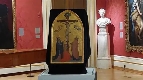 BBC The Crucifixion with the Virgin, Saint John the Evangelist and the Magdalen by Fra Angelico in a room at the Ashmolean Museum in Oxford. A sculpture and other paintings can be seen behind it.