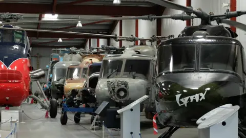 The Helicopter Museum A row of helicopters in a large hangar with information boards in front of each exhibit