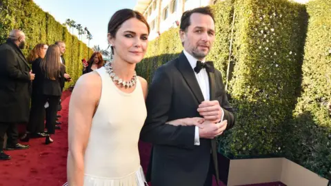 Getty Images Keri Russell, left, and Matthew Rhys at the 81st Golden Globe Awards held at the Beverly Hilton Hotel on January 7, 2024 in Beverly Hills, California.
She is wearing a white dress and necklace, he is in a black dinner suit and bowtie.