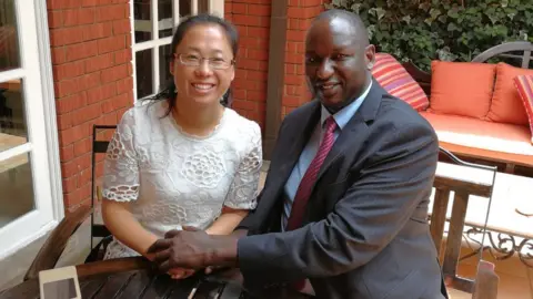 BBC Xu Jing and Henry Rotich hold hands as they sit at a table