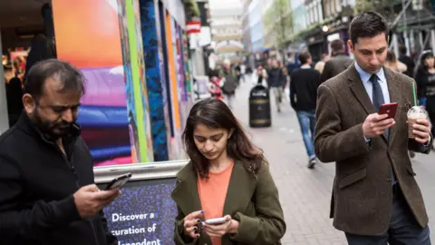 Getty Images Shoppers look at their mobile phones