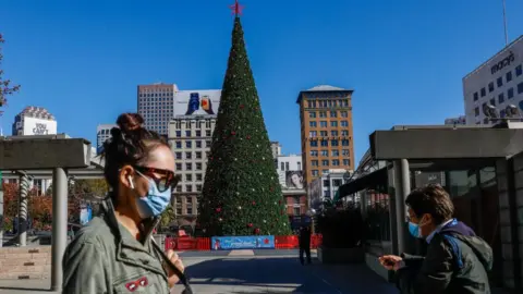 Getty Images People walk through a quiet Union Square, past a Christmas tree, in San Francisco, California on 1 December 2020