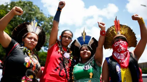 Getty Images Four indigenous women raise their hands as they call for gender equality during a protest in Brasilia on International Women's Day, on March 8, 2020.