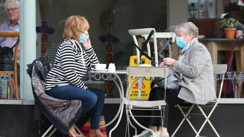 PA Media Women wearing facemasks outside a cafe
