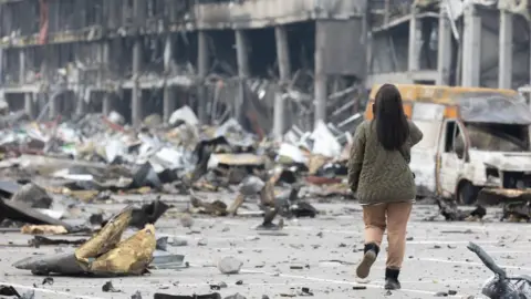 SOPA Images Women with mobile phone waling through war rubble.