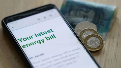 PA Media A mobile phone displaying an energy bill, with coins and a £5 note sitting next to it