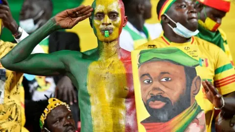 Getty Images A Mali supporter holds a portrait of Malian junta leader Colonel Assimi Goita before the Africa Cup of Nations (CAN) 2021 round of 16 football match between Mali and Equatorial Guinea at Limbe Omnisport Stadium in Limbe on January 26, 2022