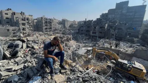 Reuters A man sits atop a pile of rubble following an Israeli strike on the Gaza Strip