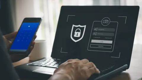 Getty Images Phishing scam, mobile phone hacker, or cyber scam concept. Password and login passcode in the smartphone. Online security threat and fraud. a scammer with cell phone and laptop. Bank account security.