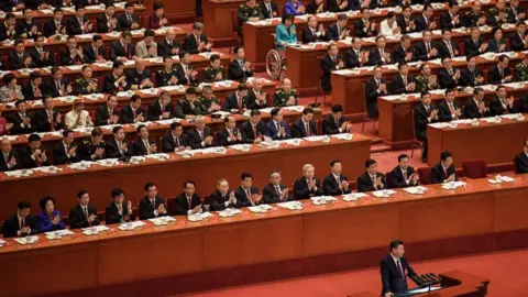 Getty Images Delegates applaud a speech by President Xi Jinping at China's Communist Party Congress in Beijing. Most are men in dark suits, with a handful of women dotted around.