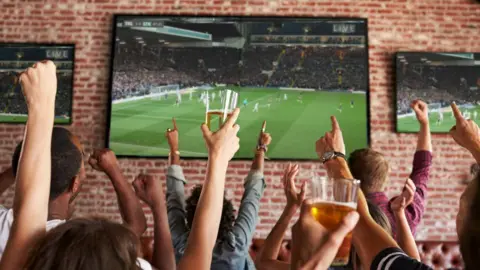 Getty Images Rear view of people in a sports bar watching football on screens