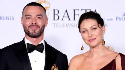 PA Media Matt Willis and Emma Willis at the BAFTA TV Awards 2024. Matt Willis is wearing a black tuxedo with a bow tie. Emma Willis is wearing an off the shoulder red dress. Both are smiling at the camera.
